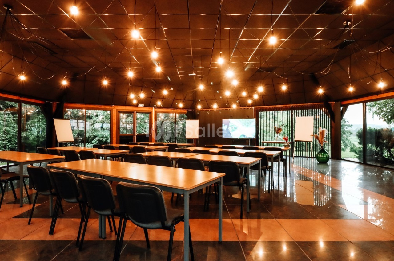 Salle de réunion lumineuse avec des tables, chaises, écrans et grandes baies vitrées donnant sur un espace vert.
