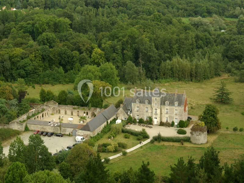 Vue aérienne d'un manoir entouré de verdure, avec des bâtiments annexes et un parking à proximité.
