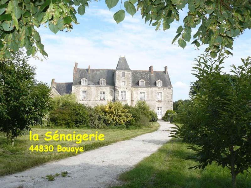 Manoir en pierre entouré de verdure, avec un chemin menant à l'entrée principale, sous un ciel dégagé.