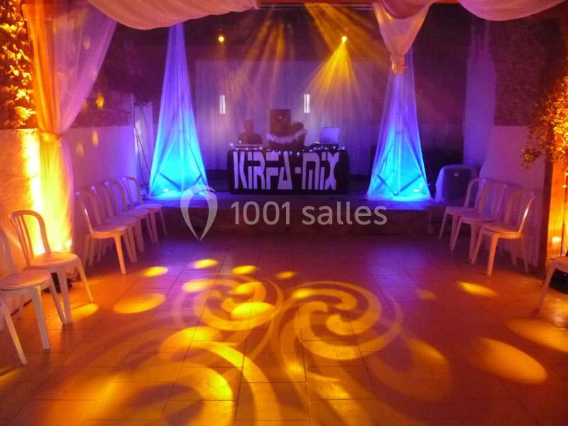 Salle de réception éclairée avec des jeux de lumières colorés, une scène avec une table de mixage au fond.