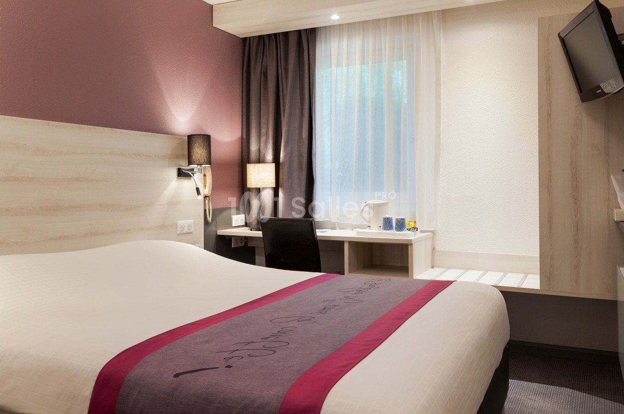 Chambre d'hôtel avec lit double, bureau, chaise, télévision murale et fenêtre avec rideaux.