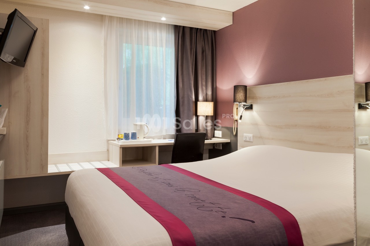 Chambre d'hôtel avec lit double, bureau, chaise, lampe, télévision et fenêtre avec rideaux.