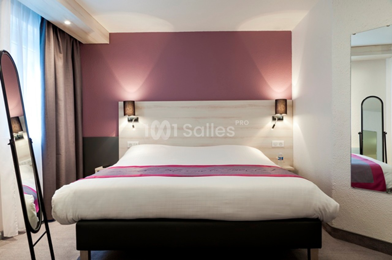 Lit double avec draps blancs dans une chambre moderne aux tons roses et neutres, éclairée par des appliques murales.