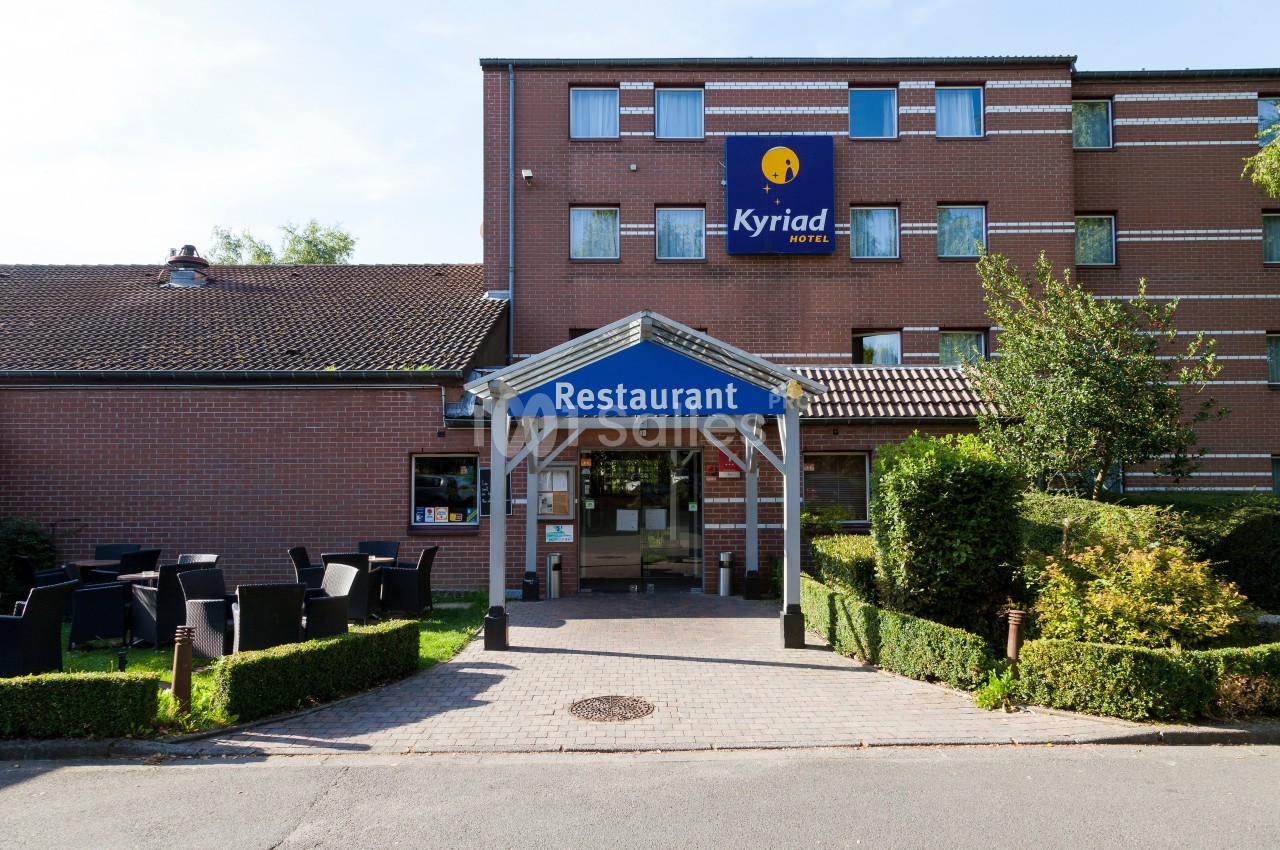 Entrée d'un hôtel-restaurant en briques rouges avec terrasse extérieure et enseigne visible.