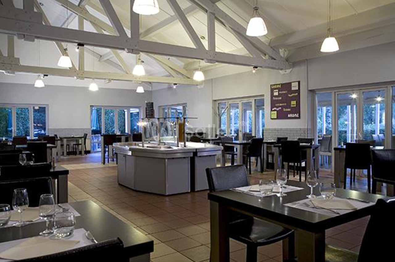 Salle de restaurant lumineuse avec tables dressées, chaises noires et un buffet central sous un plafond en poutres…
