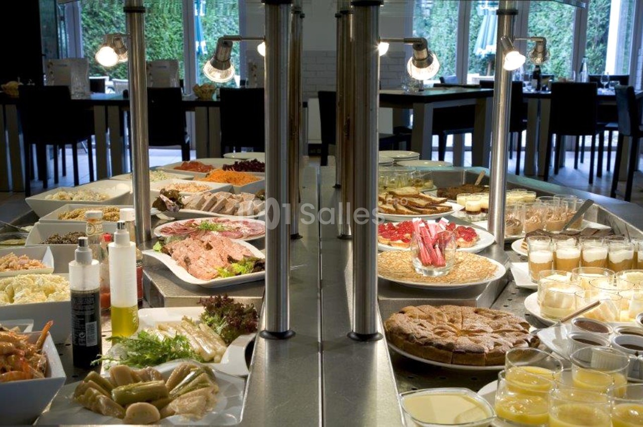 Buffet varié avec plats froids, desserts, salades et condiments disposés sur une table dans un restaurant lumineux.