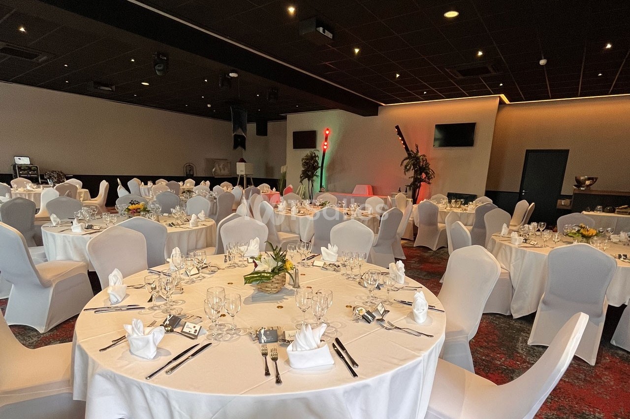 Salle de réception avec tables rondes dressées, nappes blanches, chaises assorties et décorations florales.