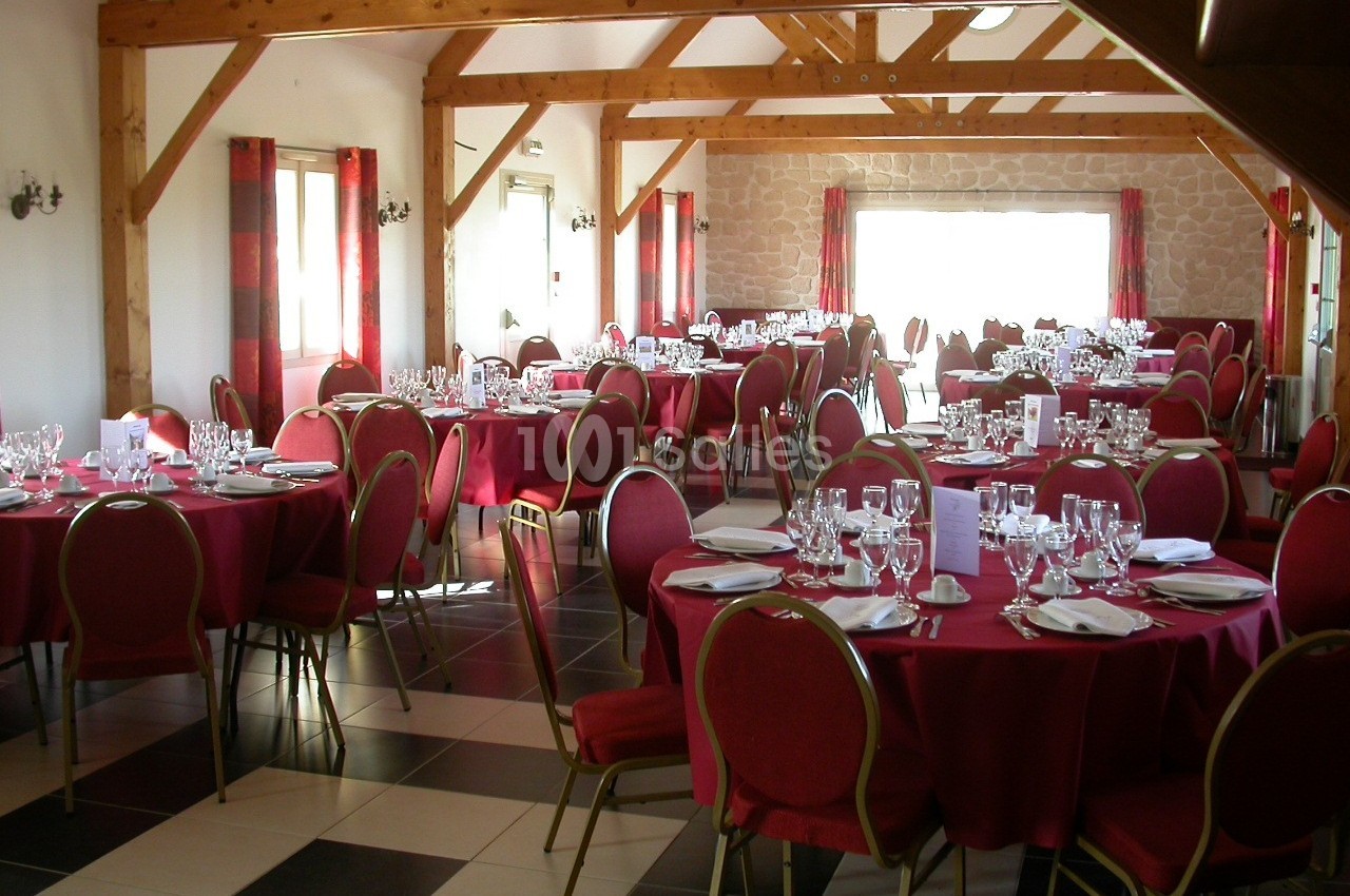 Salle de réception lumineuse avec tables rondes dressées, nappes rouges et chaises assorties.