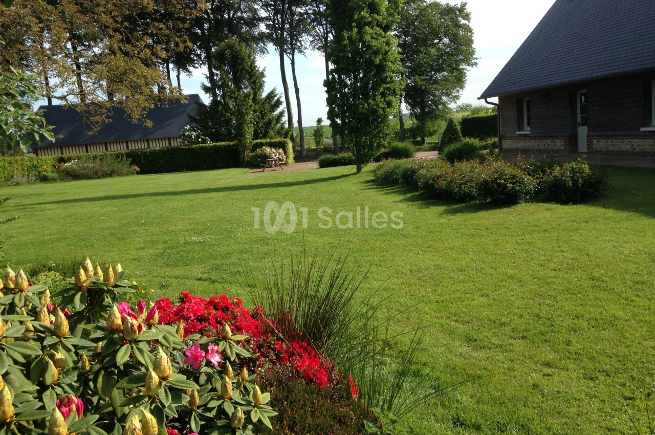 Jardin verdoyant avec pelouse, massifs fleuris et arbres, bordé par une maison en bois sous un ciel dégagé.
