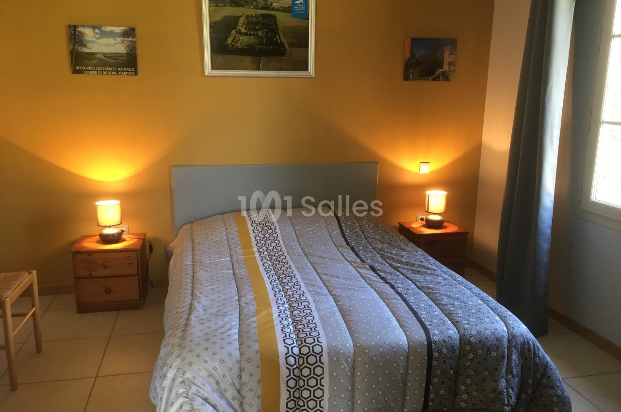 Chambre avec un lit double, deux tables de chevet éclairées par des lampes et des cadres accrochés au mur jaune.