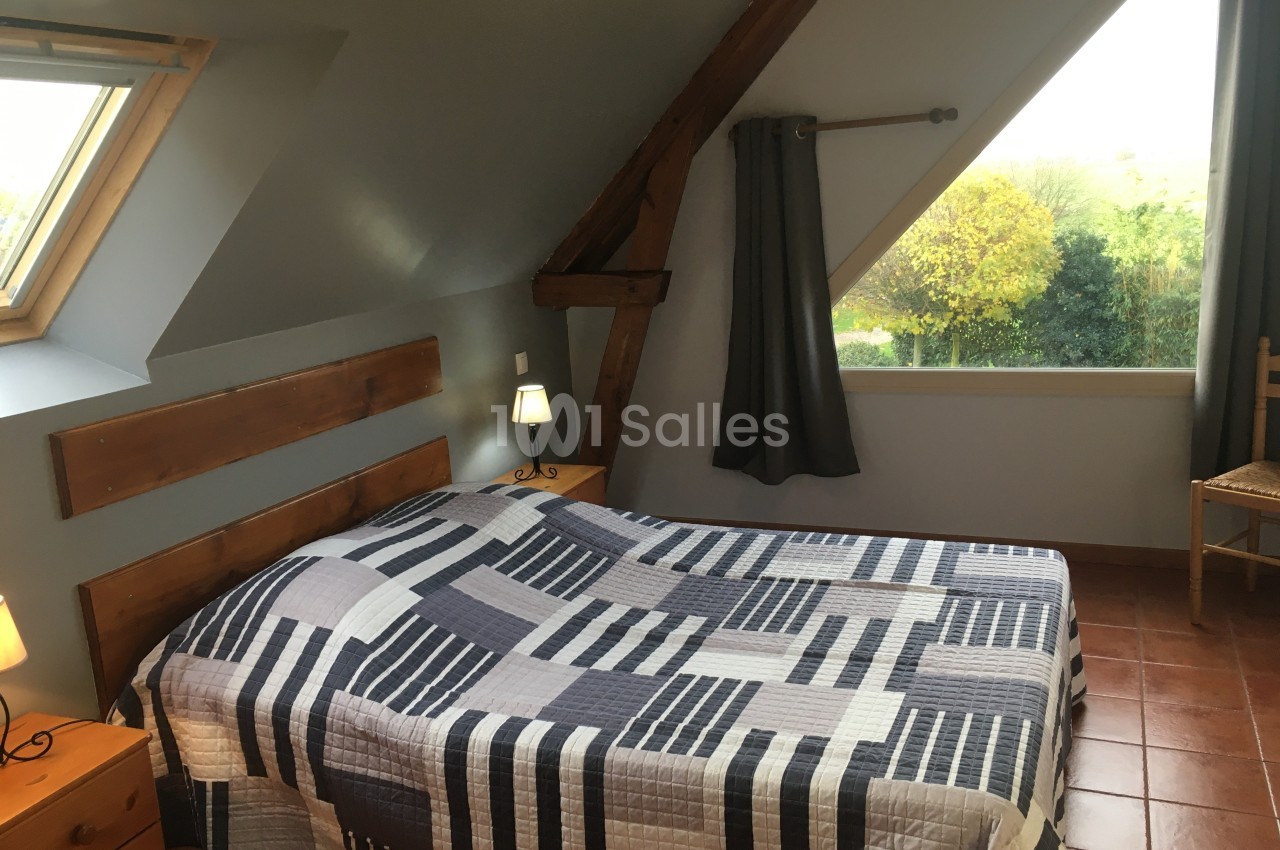 Chambre mansardée avec lit double, couvre-lit à motifs géométriques, poutres apparentes et vue sur jardin.
