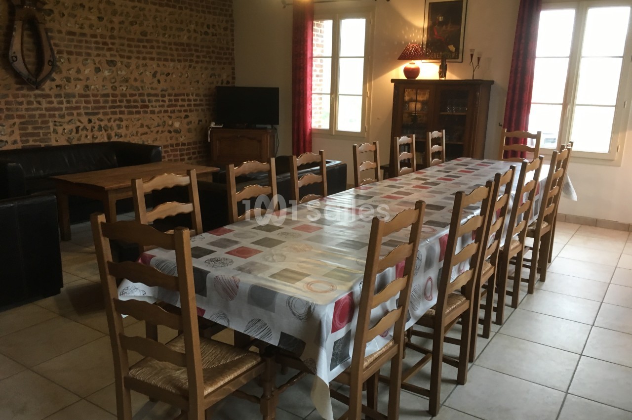 Grande table rectangulaire recouverte d'une nappe colorée, entourée de chaises en bois, dans une salle à manger lumineuse.