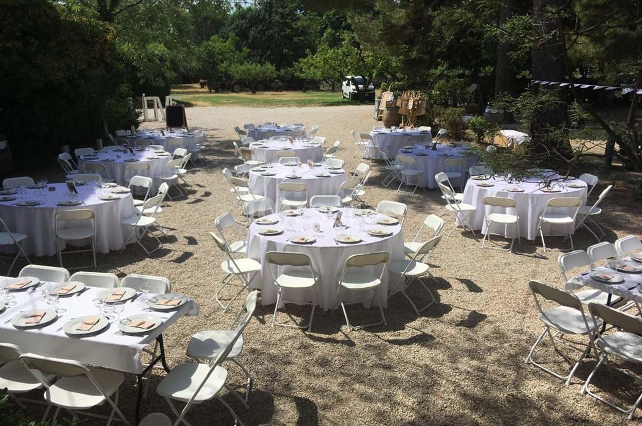 Tables rondes dressées avec nappes blanches et chaises pliantes dans un espace extérieur ombragé.