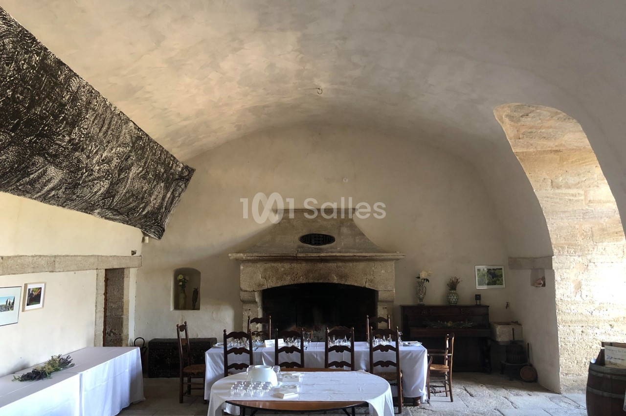 Salle voûtée ancienne avec cheminée en pierre, tables dressées avec nappes blanches et décorations simples.