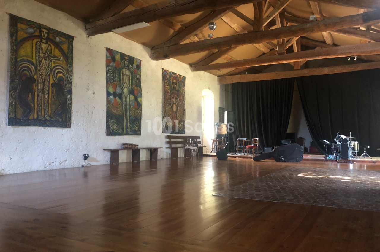 Salle spacieuse avec parquet en bois, poutres apparentes, tapis, tableaux colorés et instruments de musique installés.