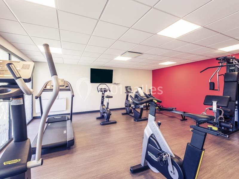 Salle de sport lumineuse avec tapis de course, vélos d'appartement et équipements de musculation.
