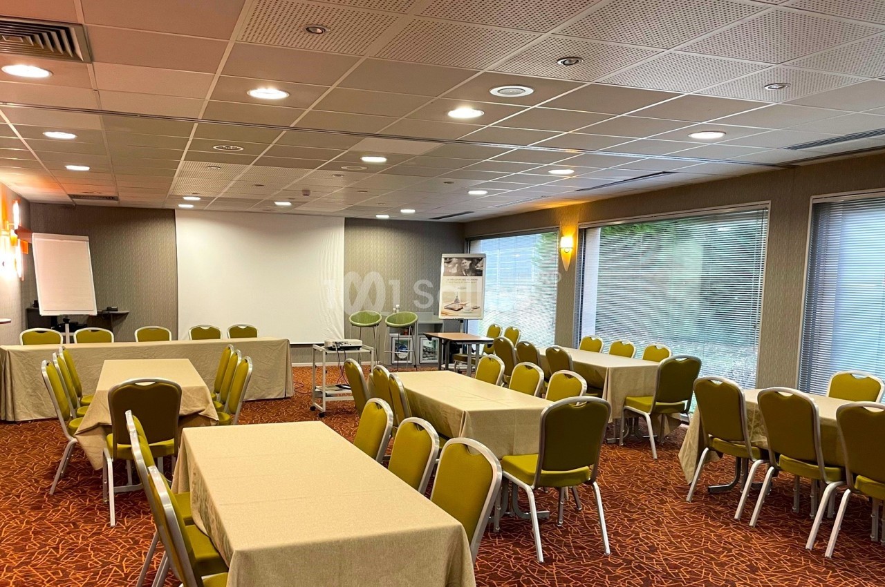 Salle de réunion lumineuse avec tables rectangulaires couvertes de nappes beige, chaises vertes et équipement de…