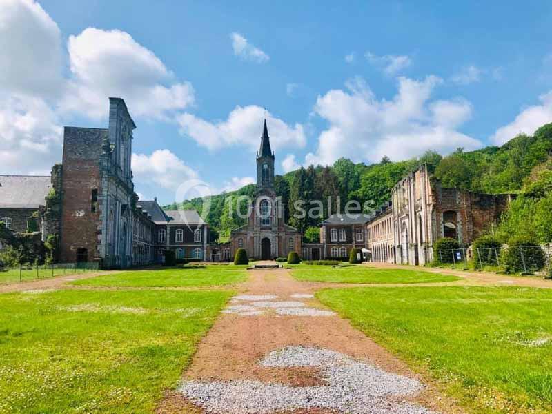 Vue d'une abbaye en ruines entourée de verdure sous un ciel partiellement nuageux.