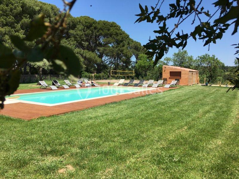 Piscine extérieure entourée de transats sur une terrasse en bois, située dans un grand jardin verdoyant.