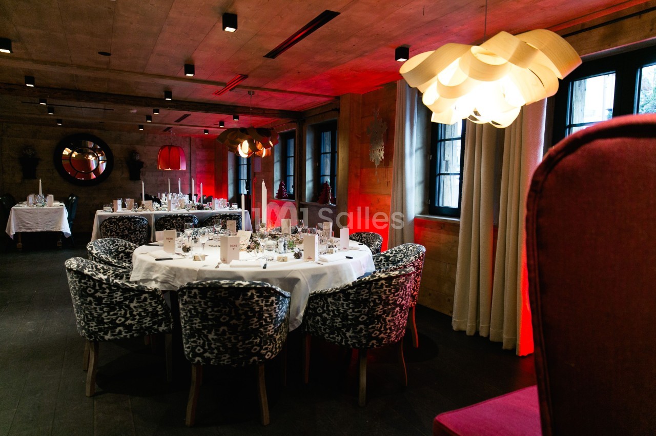 Salle de réception élégante avec tables rondes dressées, chaises à motifs et éclairage tamisé.