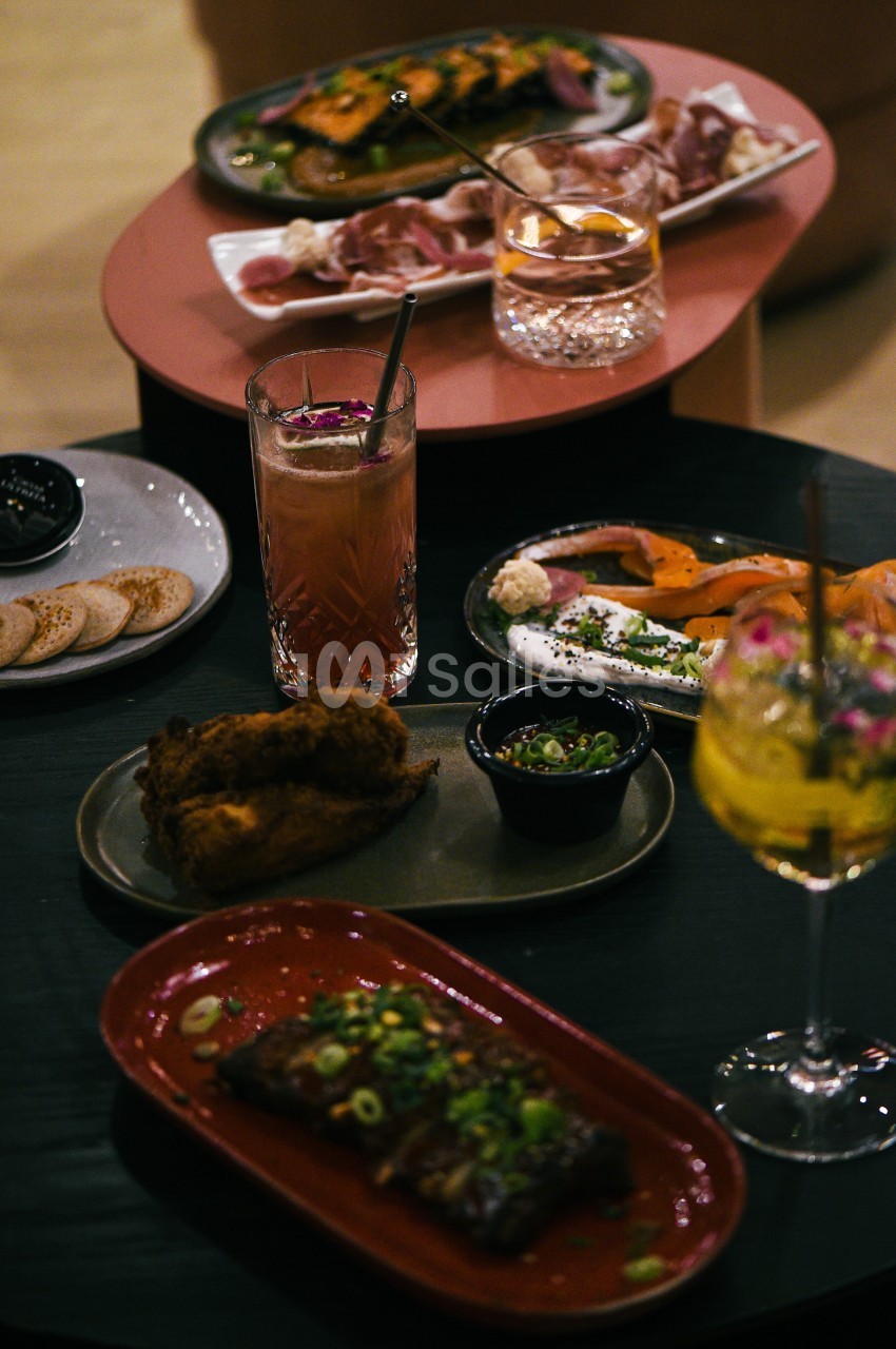 Assortiment de plats et cocktails sur des tables, incluant viande, poisson fumé, pain et accompagnements.