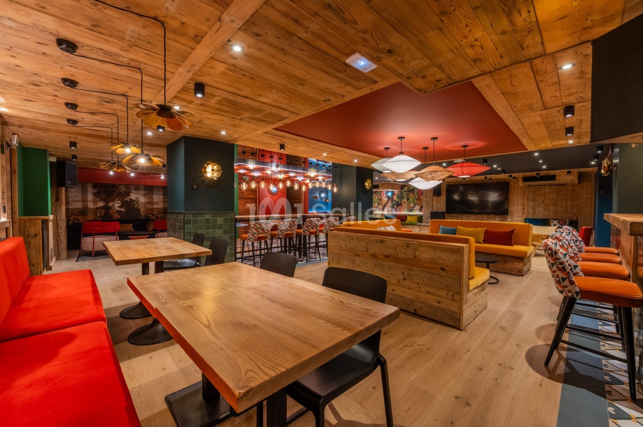 Salle moderne avec tables en bois, banquettes colorées, éclairage suspendu et décoration chaleureuse en bois.
