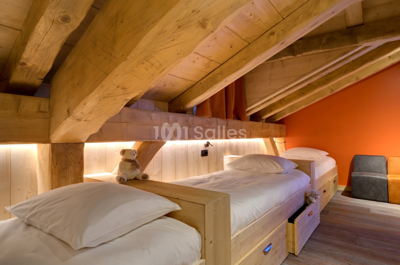 Chambre mansardée avec deux lits simples en bois, éclairage doux et murs en bois et orange.