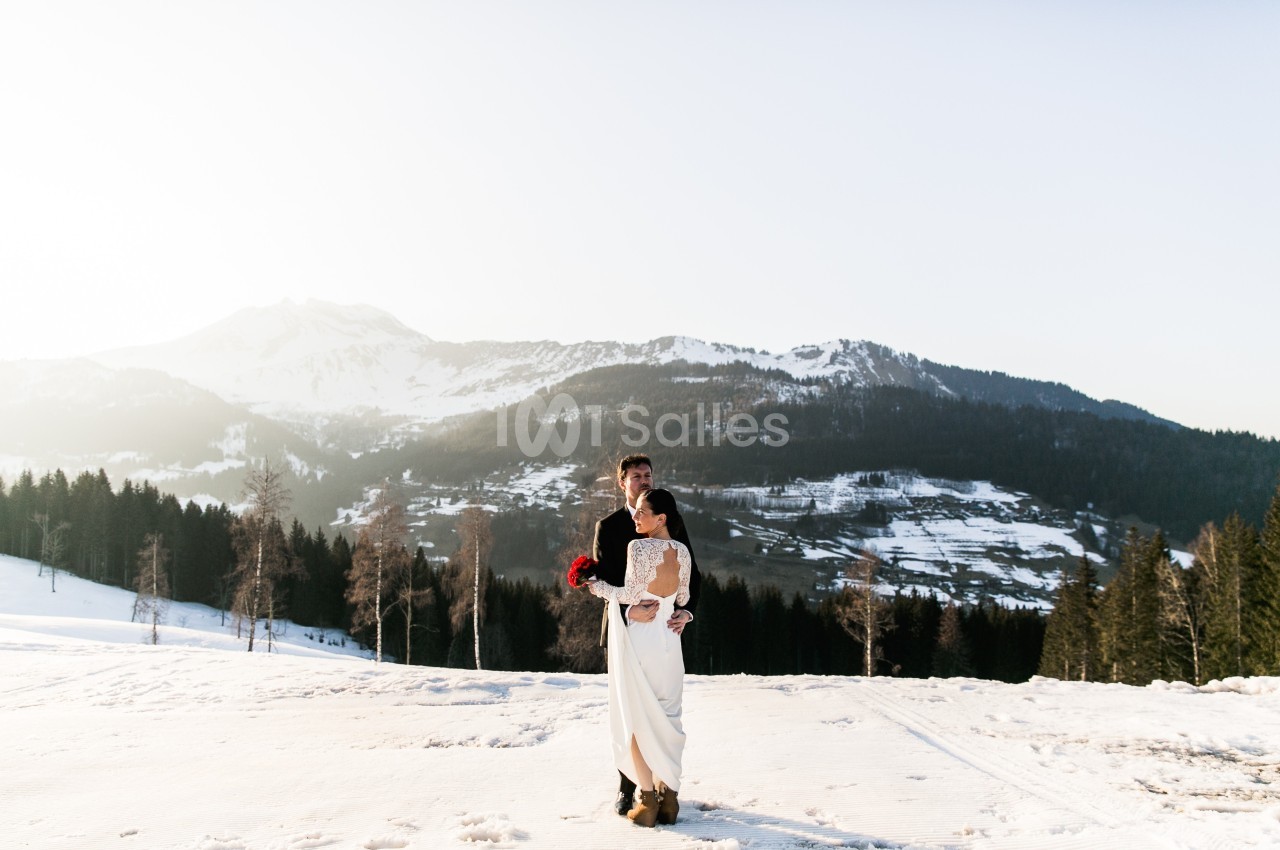 Un couple en tenue de mariage pose dans un paysage enneigé avec des montagnes en arrière-plan.