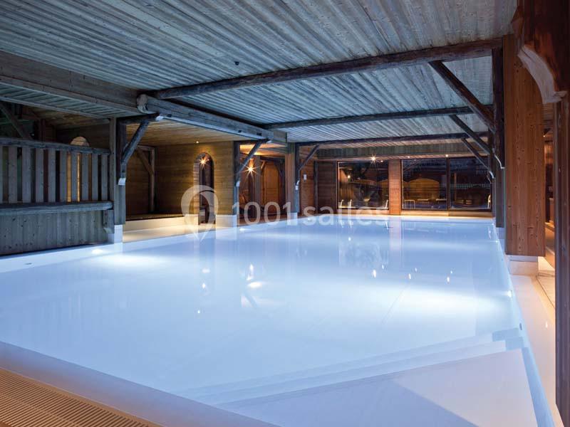 Piscine intérieure éclairée sous un plafond en bois avec des poutres apparentes et des murs en bois.
