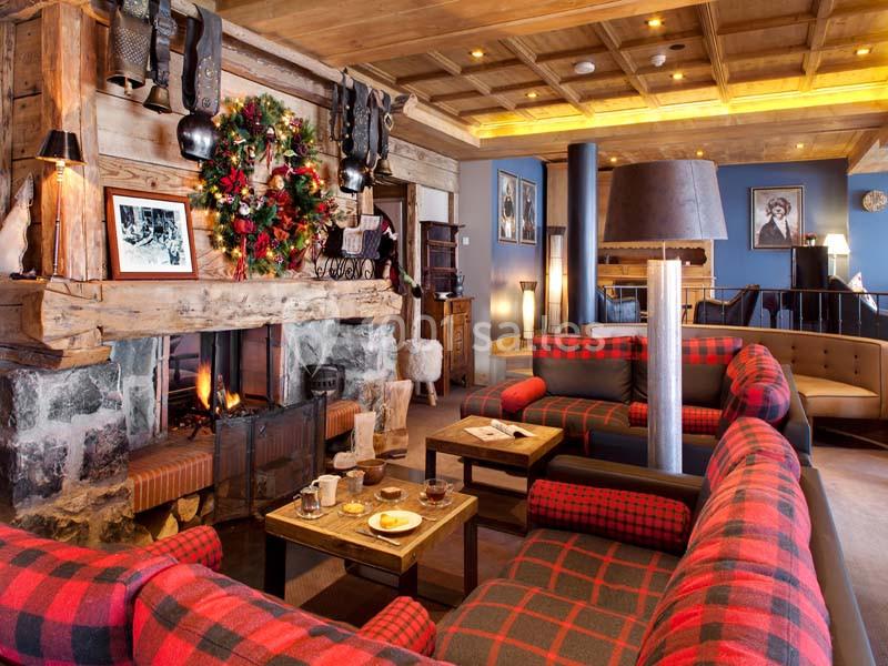 Salon chaleureux avec cheminée allumée, décorations de Noël, canapés à carreaux rouges et tables en bois.