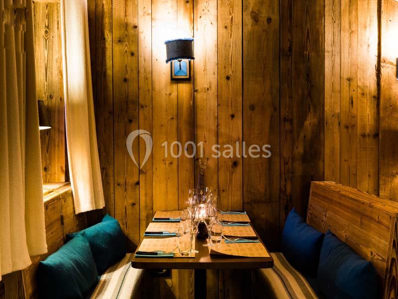 Table en bois dressée pour quatre personnes dans un intérieur chaleureux avec des murs en bois et un éclairage tamisé.