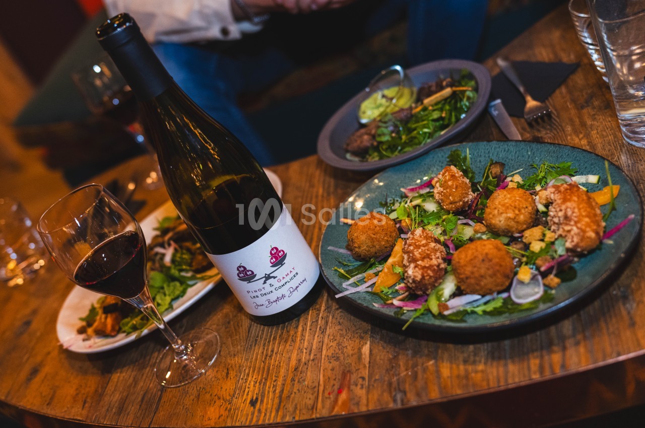 Assiette de croquettes avec salade, verre de vin rouge et bouteille posés sur une table en bois.