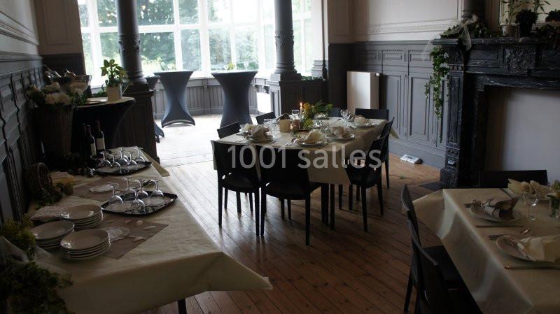 Salle lumineuse avec tables dressées pour un repas, décorée de plantes et baignée de lumière naturelle.