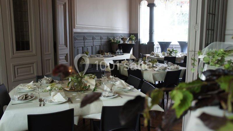 Salle de réception élégante avec tables dressées, nappes blanches, vaisselle raffinée et décoration végétale.
