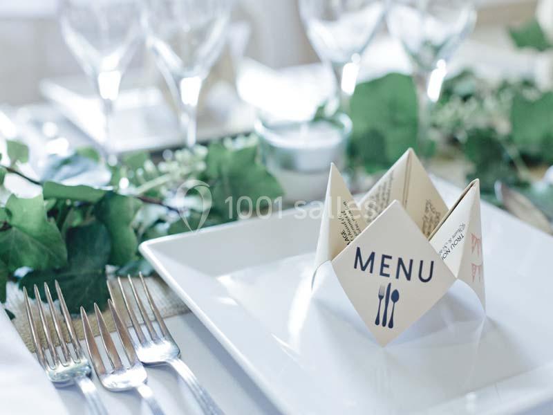 Serviette pliée en forme de cocotte avec l'inscription ’Menu’ sur une table élégamment dressée avec verres et couverts.