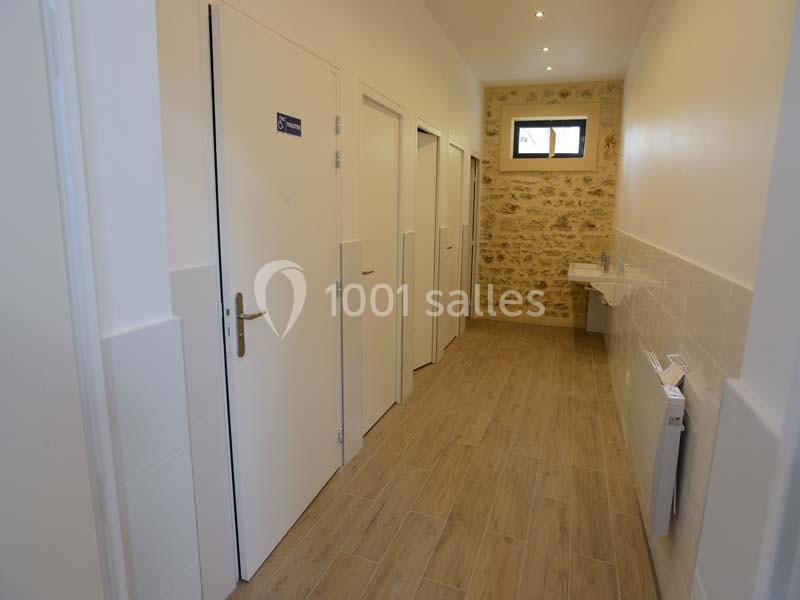 Couloir avec plusieurs portes blanches, un mur en pierre apparente, un lavabo et un éclairage au plafond.