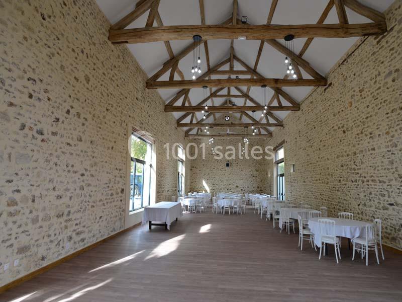 Salle lumineuse avec murs en pierre, poutres apparentes, tables rondes dressées et grandes fenêtres laissant entrer la…