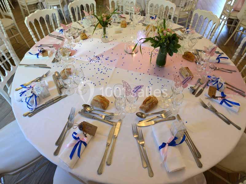 Table ronde décorée pour un événement avec nappes blanches, couverts, fleurs, rubans et petits pains.