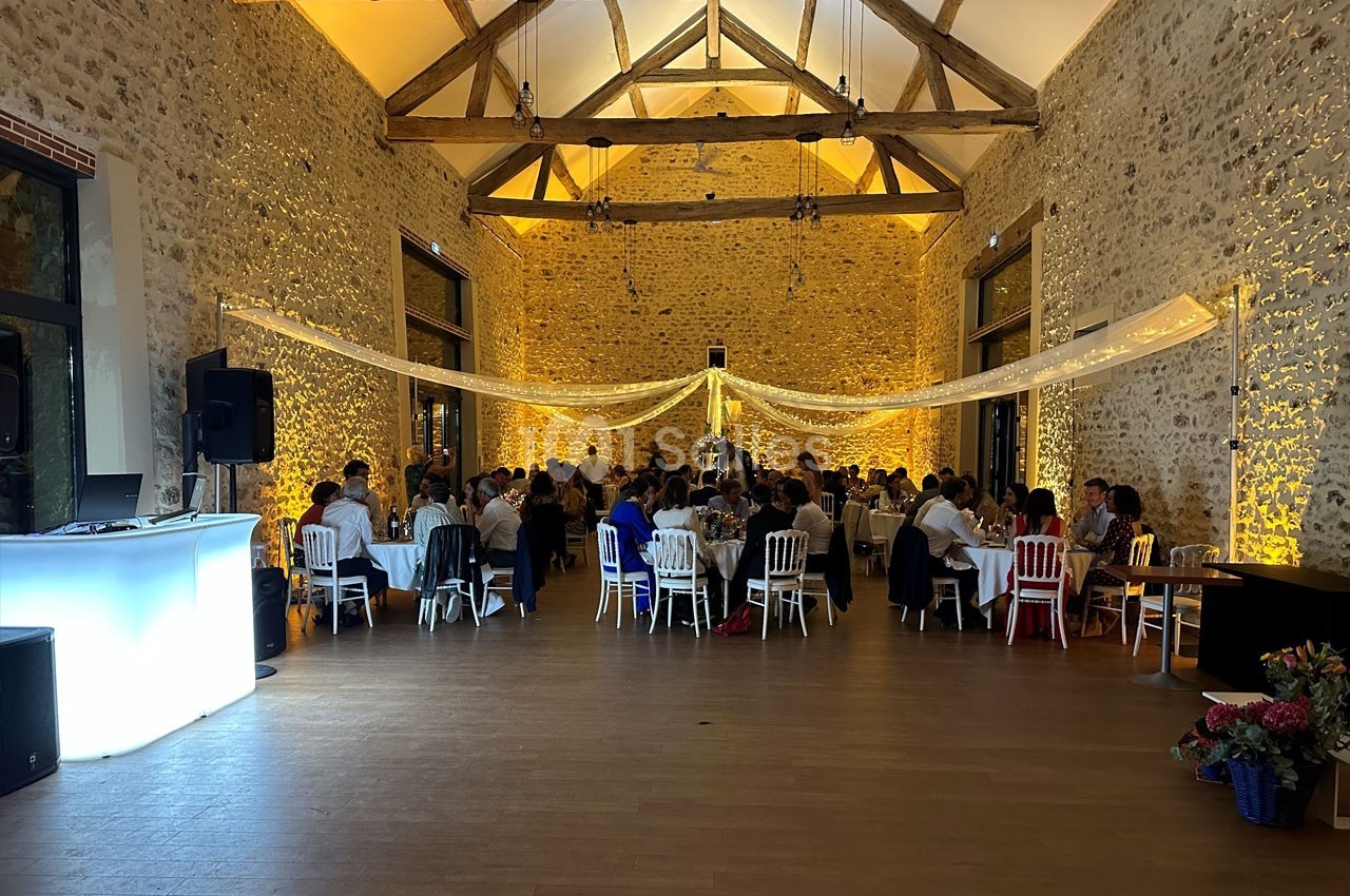 Salle de réception en pierre avec des invités assis à des tables, éclairage chaleureux et décoration lumineuse suspendue.