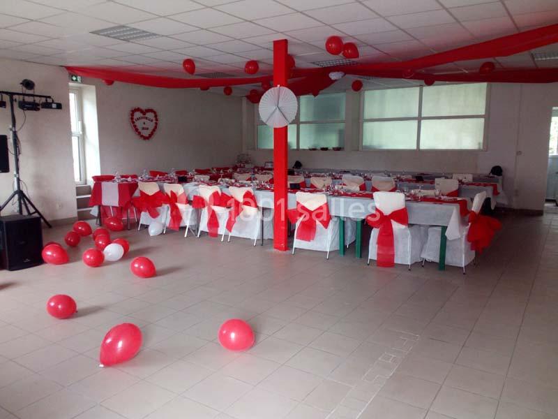 Salle décorée en rouge et blanc avec des tables alignées, des chaises ornées de nœuds et des ballons au sol.