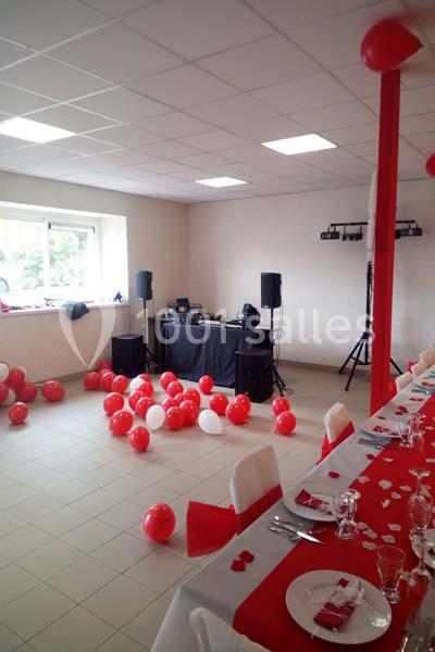 Salle décorée en rouge et blanc avec ballons, table dressée et matériel de sonorisation installé près d'une fenêtre.