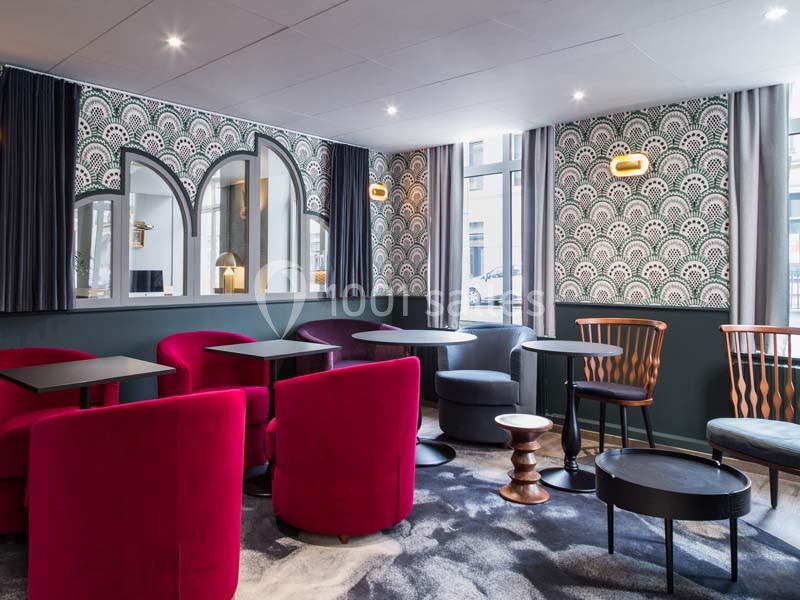 Salle de détente avec fauteuils rouges, tables basses et murs décorés de motifs géométriques.