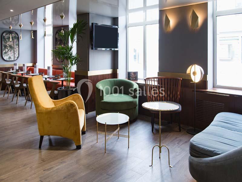 Espace intérieur lumineux avec fauteuils colorés, tables basses et grandes fenêtres laissant entrer la lumière naturelle.