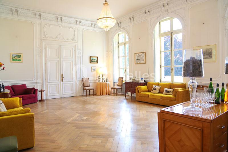 Salon lumineux avec parquet en bois, canapés colorés, lustre central et grandes fenêtres donnant sur l'extérieur.