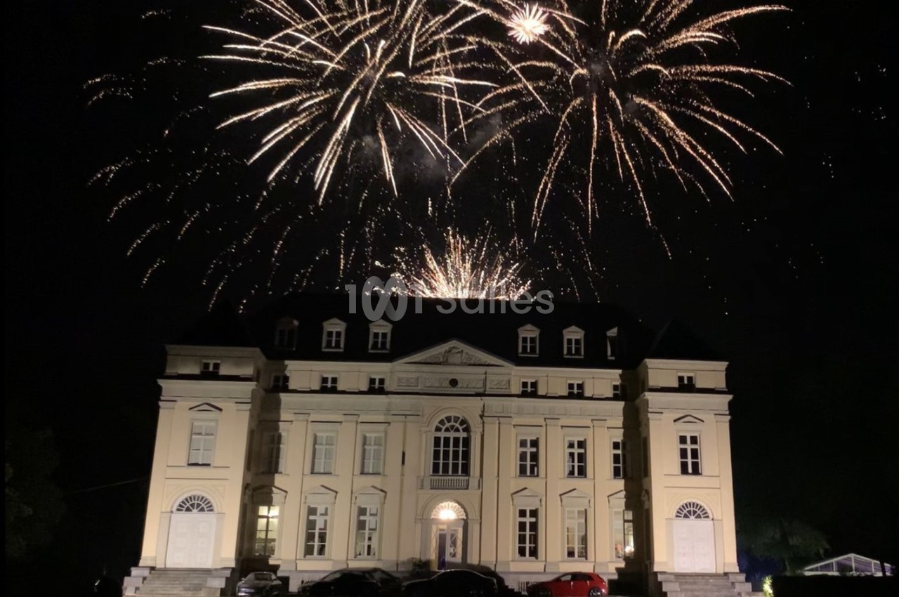 Feu d'artifice illuminant le ciel nocturne au-dessus d'un grand bâtiment de style classique.