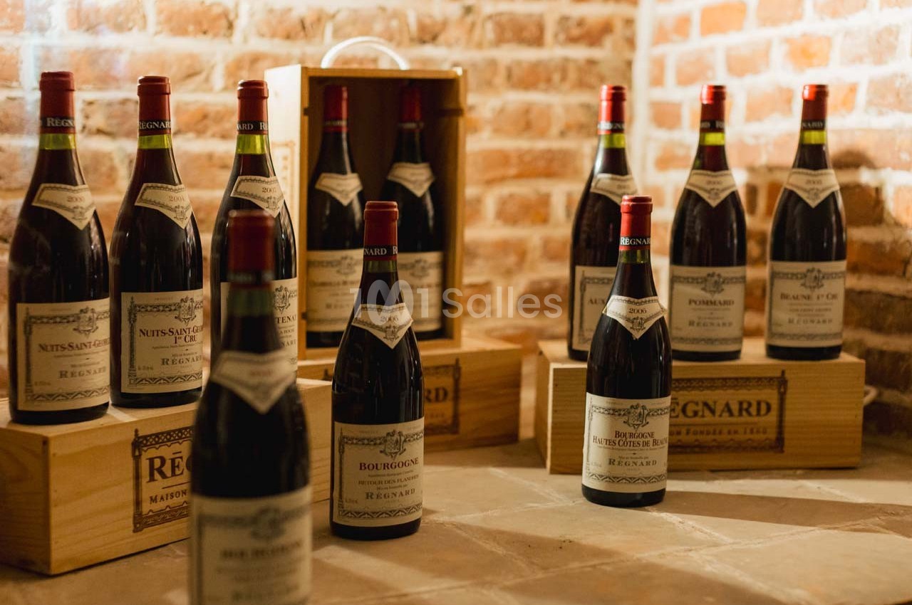 Bouteilles de vin rouge disposées sur des caisses en bois dans une cave aux murs de briques.