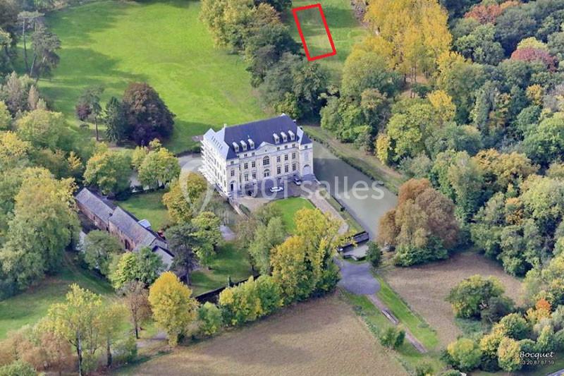 Vue aérienne d'un château entouré de verdure, avec un plan d'eau et des bâtiments annexes à proximité.