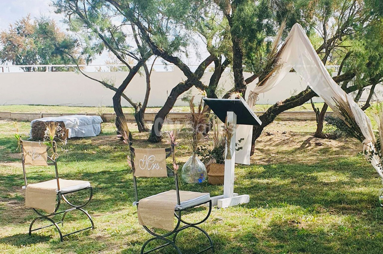 Chaises décorées et pupitre installés en extérieur sous des arbres, avec un voile suspendu en arrière-plan.