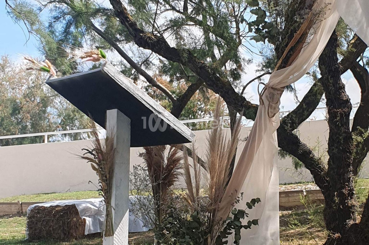 Un pupitre en bois décoré de fleurs séchées, placé en extérieur près d'un arbre avec des voilages suspendus.