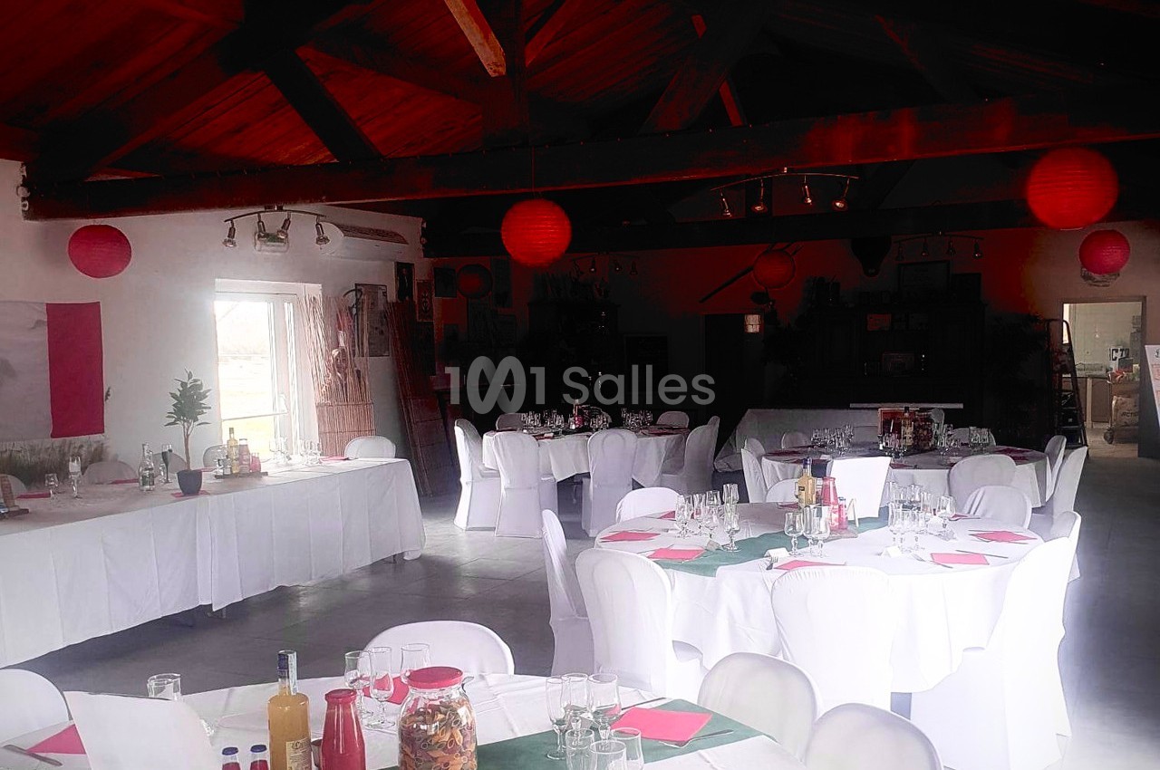 Salle de réception décorée avec des tables rondes dressées, nappes blanches et lanternes rouges suspendues.